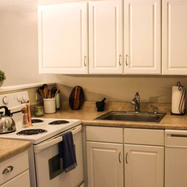 View of a kitchen with a white stove and stainless steel sink with white cabinets.